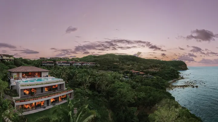 Villa Taiyari lit at dusk on the hillside of Punta Mita, the pool glowing on its top terrace and the coast beyond