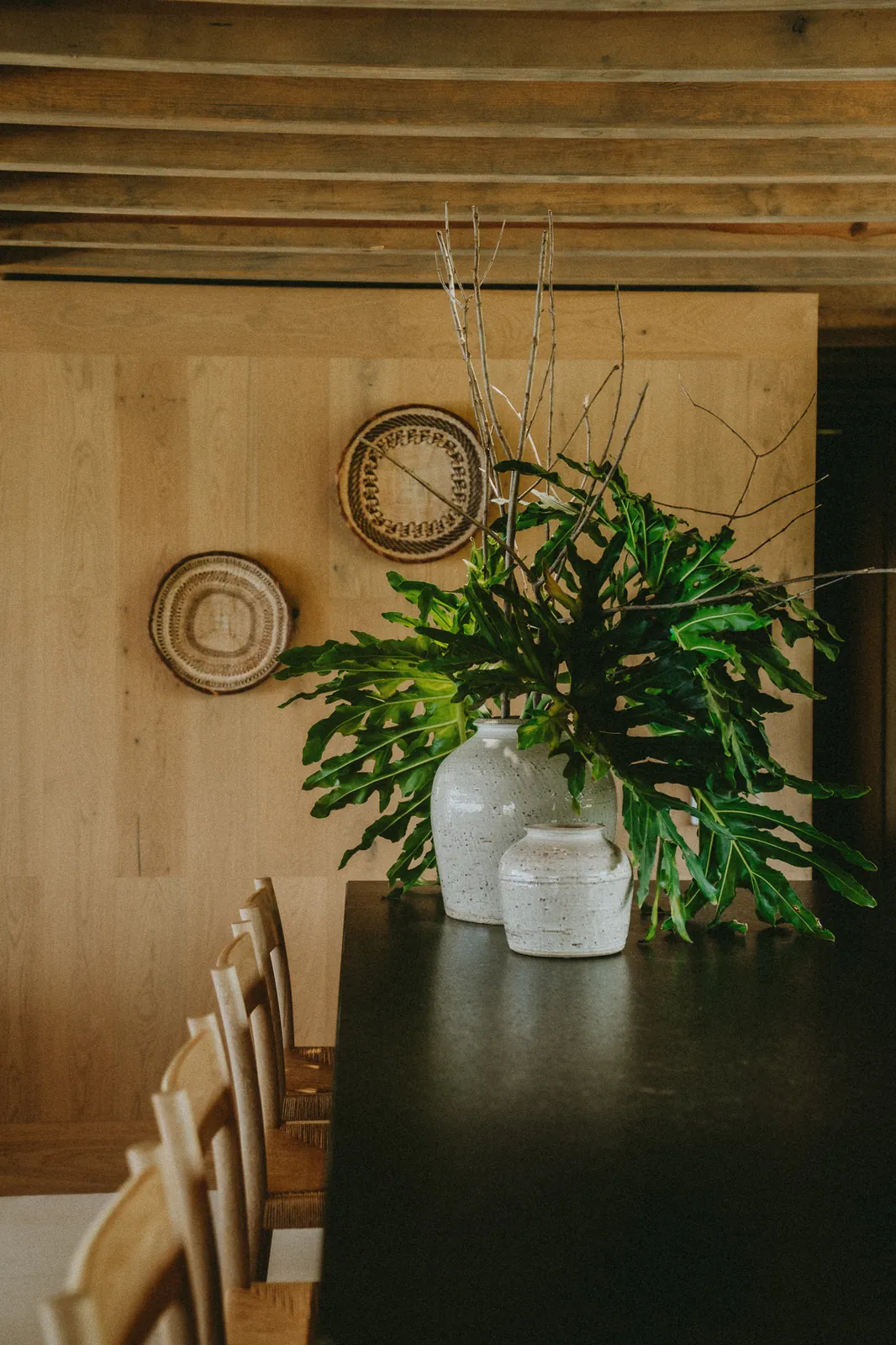 Ceramic vases and tropical leaves on a dark counter, woven baskets hung on the wood-panelled wall