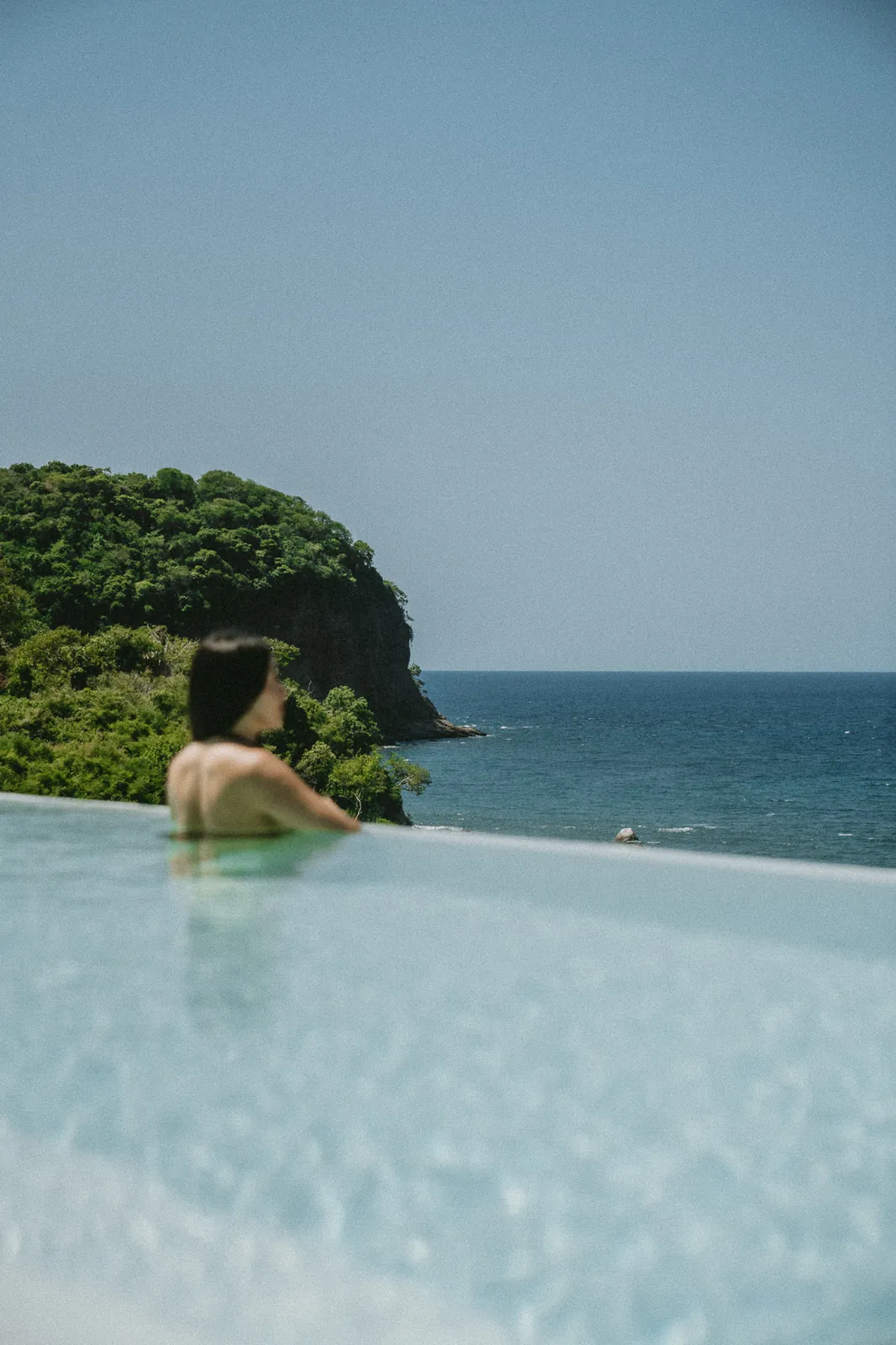 A swimmer at the edge of the infinity pool, looking out to a green headland and the ocean